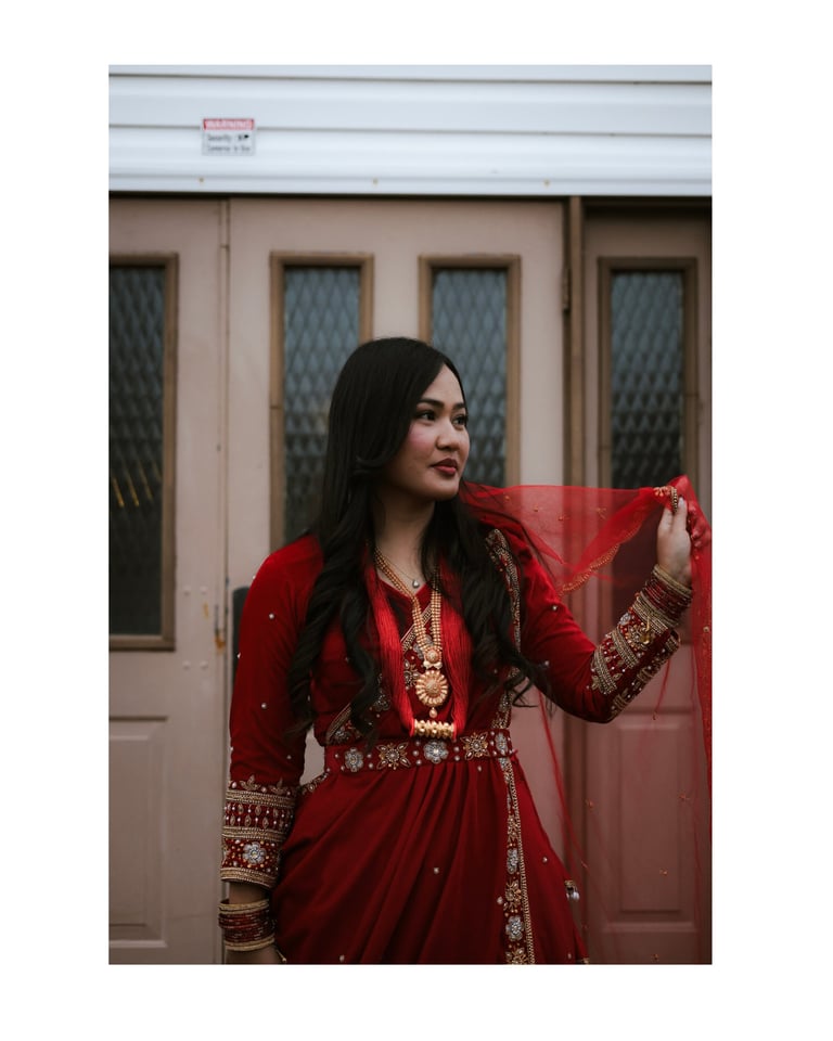 Woman in red embroidered traditional dress holding red fabric against beige building with windows