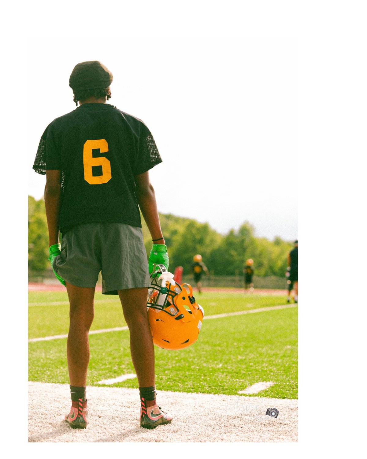 Football player wearing number 6 jersey standing on field holding orange helmet