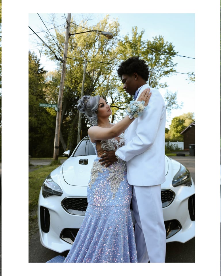 Couple in formal attire posing together in front of a white sports car on a tree-lined street