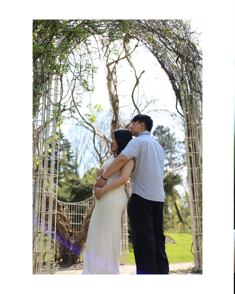 Couple embracing under a wooden archway decorated with vines and flowering branches in a garden setting
